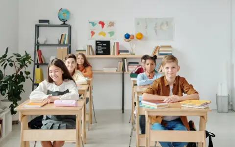 Schüler sitzen an Holztischen. Eine Lehrerin könnte hier kreative Sitzordnung Grundschule Ideen umsetzen.
