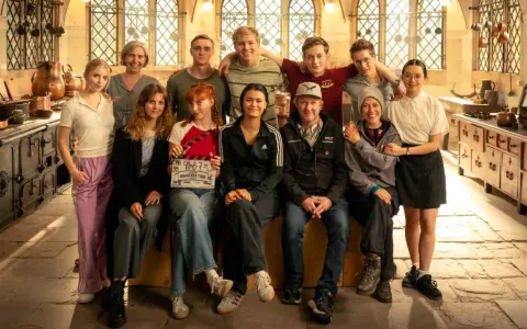 Das Team von "Die Schule der magischen Tiere" posiert in einer historischen Küche. Ein Mädchen hält eine Klappe mit dem Titel.