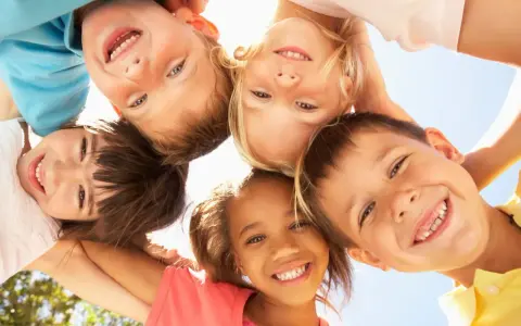 Fünf lachende Kinder blicken von oben in die Kamera. Sie zeigen, wie einfach es ist, Freunde in der Schule zu finden: mit einem Lächeln!