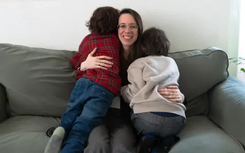 Eine Frau umarmt liebevoll zwei Kinder auf einer Couch. Ein Beispiel, wie man mit ADHS umgehen kann: durch Geborgenheit und Verständnis.