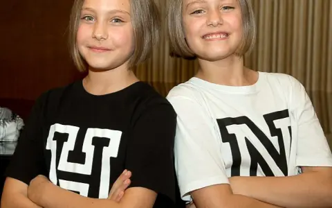 Zwei Mädchen mit kurzen Haaren, die T-Shirts mit den Buchstaben "H" und "N" tragen. Man fragt sich, wie alt sind Hanni und Nanni wohl?