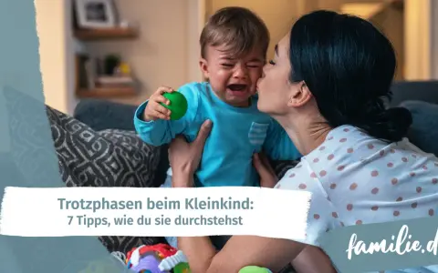 Mutter tröstet weinendes Kind, das einen grünen Ball hält. Ein Beispiel für den emotionalen quotient eines Kleinkindes.