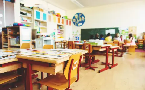 Leere Schultische und Stühle in einem Klassenzimmer, bereit für eine sitzordnung unruhige klasse. Kinder sitzen im Hintergrund.