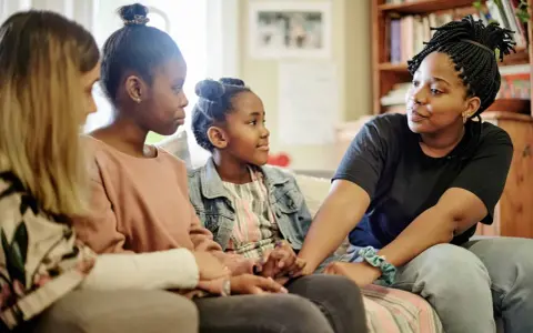 Eine Familie spricht auf dem Sofa. Das jüngste Kind, das oft als hyperaktives Kind beschrieben wird, hört aufmerksam zu.