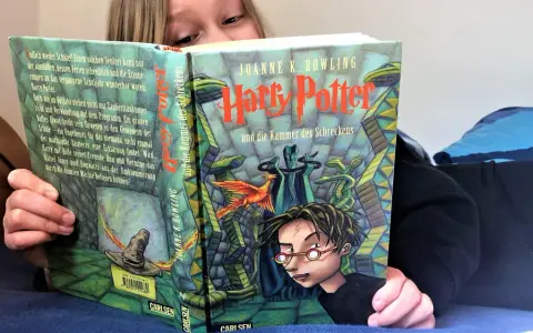 Ein Kind liest Harry Potter und die Kammer des Schreckens, eine Harry Potter Kinderversion. Der Zauberhut und ein Phönix sind auf dem Cover zu sehen.