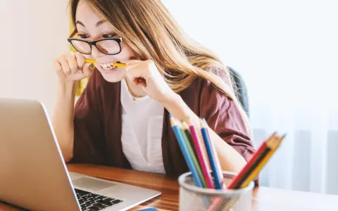 Junge Frau mit Brille bei der Arbeit, kaut auf einem Bleistift. Sie repräsentiert verschiedene lerntypen, die sich auf unterschiedliche Weise konzentrieren.