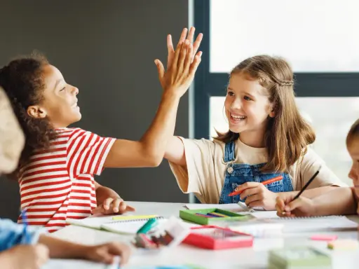 Zwei Grundschülerinnen geben sich einen High-Five, während sie konzentriert lernen. Ein tolles Beispiel für förderunterricht Grundschule, bei dem Spaß und Erfolg Hand in Hand gehen.