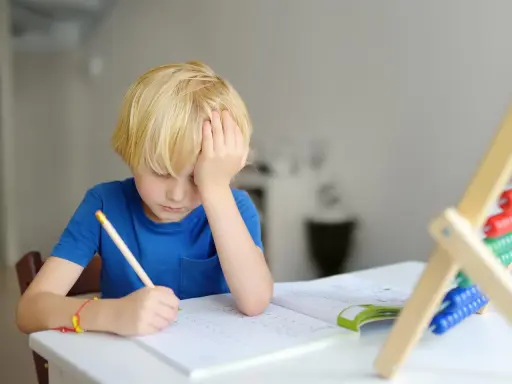 Junge mit blonden Haaren kämpft mit den Hausaufgaben. Mögliche ADHS-Ursachen und Erziehung sind hier ein Thema.