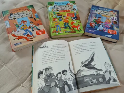 Drei Bücher der Reihe "Die Schule der magischen Tiere" von Margit Auer liegen nebeneinander. Aufgeschlagen ist ein Band mit einem Krokodil und einem Jungen.