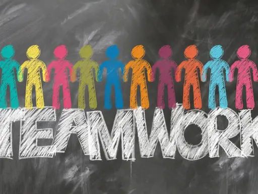 Bunte Figuren stehen auf dem Wort TEAMWORK. Tolle Ideen für die Klassenlehrerstunde, die Zusammenarbeit fördern.