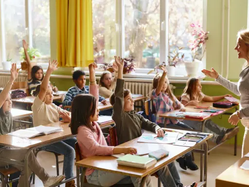 Grundschüler melden sich eifrig, ihre Sitzordnung zur Wand hin ausgerichtet, während die Lehrerin lächelt.