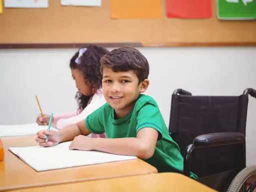 Ein Junge im Rollstuhl lächelt, während er im Unterricht schreibt. Dies ist ein Beispiel für **Inklusion in der Schule**.