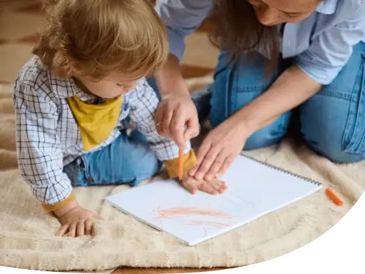 Ein Kind malt mit einem Wachsmalstift auf einem Blatt Papier, während eine Erwachsene ihm hilft. So können sie kinder motivieren mitzumachen.