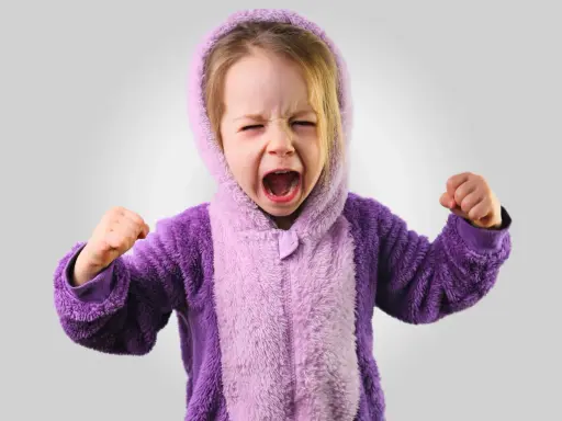 Kleines Kind im lila Pyjama schreit wütend, Fäuste geballt. Ein Ausdruck starker Emotionen bei Kindern.