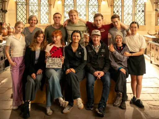 Das Team von "Die Schule der magischen Tiere" posiert in einer historischen Küche. Ein Mädchen hält eine Klappe mit dem Titel.