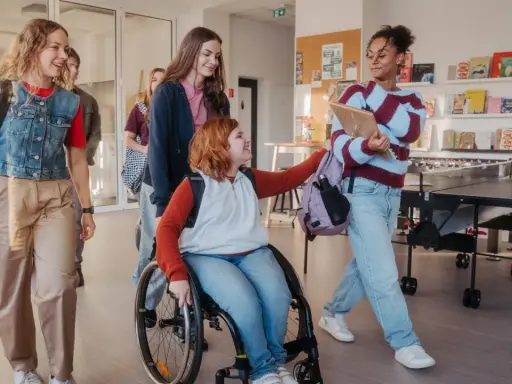 Schülerinnen gehen lachend durch den Flur. Eine im Rollstuhl, was **Inklusion an Schulen** zeigt.