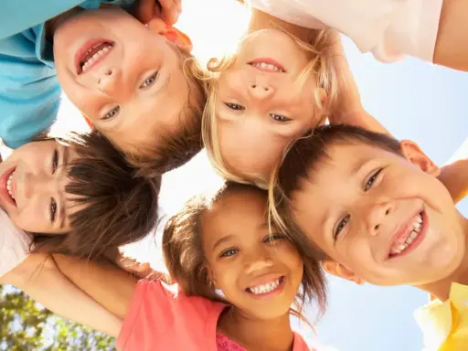 Fünf lachende Kinder blicken von oben in die Kamera. Sie zeigen, wie einfach es ist, Freunde in der Schule zu finden: mit einem Lächeln!