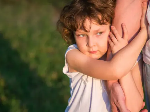 Ein Kind umklammert einen Arm, die Augen voller Kummer. Der **Trennungsschmerz bei Kindern** ist deutlich zu spüren.