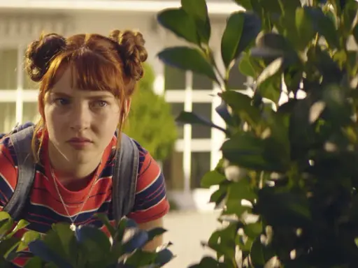 Ida aus "Die Schule der magischen Tiere" späht neugierig hinter Büschen hervor.