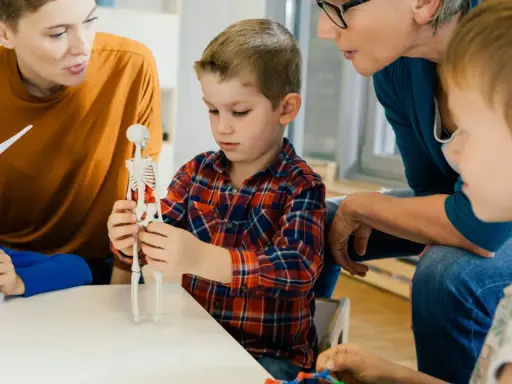 Kinder lernen mit einem Skelettmodell und einem Windrad. Die Lehrerin erklärt geduldig, wie wichtig es ist, sich auf Details zu konzentrieren, auch bei ads adhs.