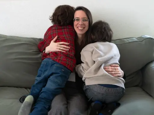 Eine Frau umarmt liebevoll zwei Kinder auf einer Couch. Ein Beispiel, wie man mit ADHS umgehen kann: durch Geborgenheit und Verständnis.
