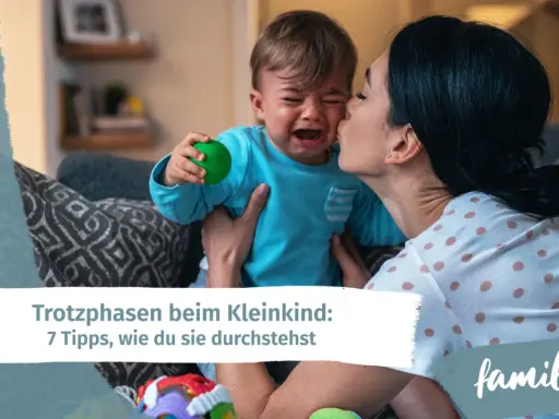 Mutter tröstet weinendes Kind, das einen grünen Ball hält. Ein Beispiel für den emotionalen quotient eines Kleinkindes.