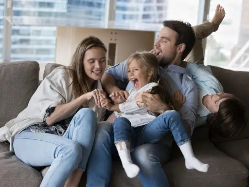 Eine Familie lacht und spielt auf dem Sofa. Das gemeinsame Lachen ist ein schönes Ritual.
