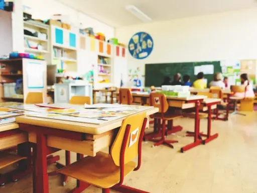 Leere Schultische und Stühle in einem Klassenzimmer, bereit für eine sitzordnung unruhige klasse. Kinder sitzen im Hintergrund.