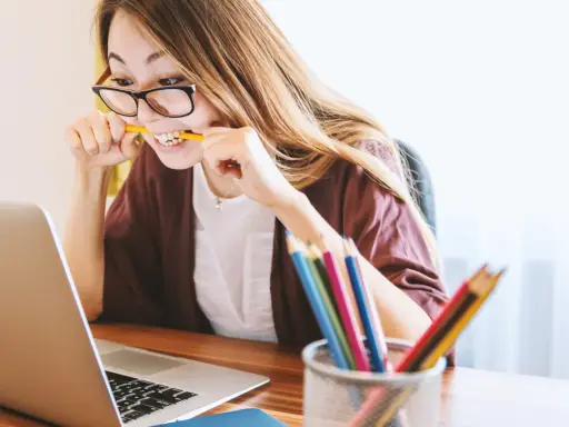 Junge Frau mit Brille bei der Arbeit, kaut auf einem Bleistift. Sie repräsentiert verschiedene lerntypen, die sich auf unterschiedliche Weise konzentrieren.