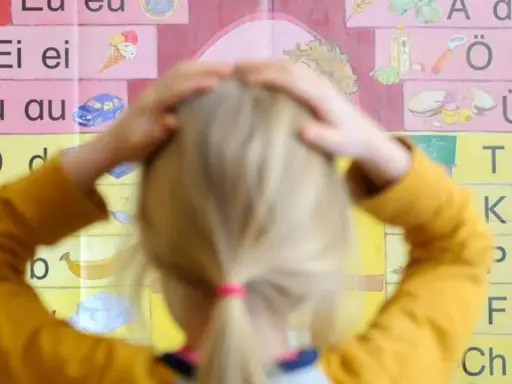 Ein Kind mit Händen am Kopf vor einer Buchstabenwand, die auf Schwierigkeiten beim Lesen und Schreiben (LRS) bei Kindern hindeuten könnte.