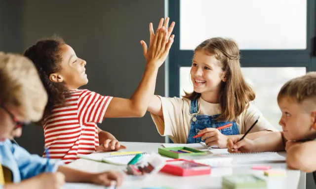 Zwei Grundschülerinnen geben sich einen High-Five, während sie konzentriert lernen. Ein tolles Beispiel für förderunterricht Grundschule, bei dem Spaß und Erfolg Hand in Hand gehen.