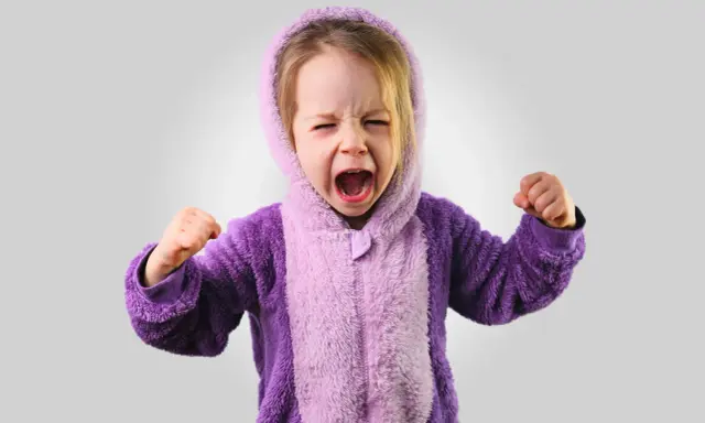 Kleines Kind im lila Pyjama schreit wütend, Fäuste geballt. Ein Ausdruck starker Emotionen bei Kindern.