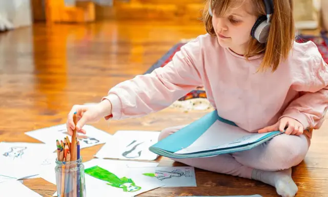 Mädchen mit Kopfhörern wählt Buntstift für Zeichnung. Kreativer Umgang mit Asperger-Kindern durch Kunst.