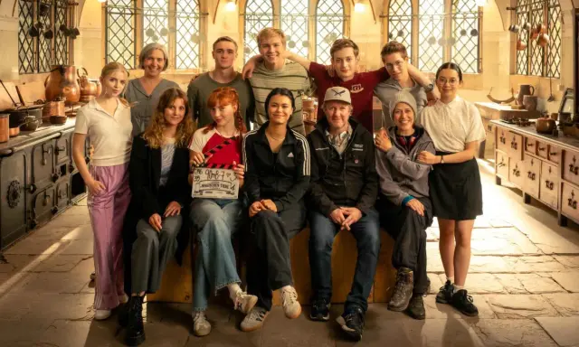 Das Team von "Die Schule der magischen Tiere" posiert in einer historischen Küche. Ein Mädchen hält eine Klappe mit dem Titel.
