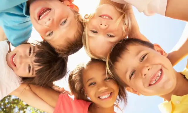 Fünf lachende Kinder blicken von oben in die Kamera. Sie zeigen, wie einfach es ist, Freunde in der Schule zu finden: mit einem Lächeln!