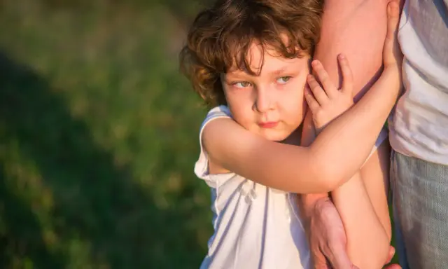 Ein Kind umklammert einen Arm, die Augen voller Kummer. Der **Trennungsschmerz bei Kindern** ist deutlich zu spüren.