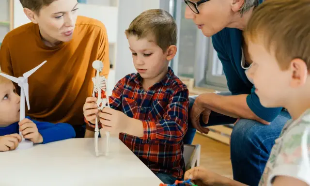 Kinder lernen mit einem Skelettmodell und einem Windrad. Die Lehrerin erklärt geduldig, wie wichtig es ist, sich auf Details zu konzentrieren, auch bei ads adhs.