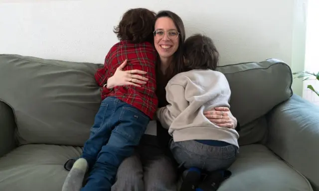 Eine Frau umarmt liebevoll zwei Kinder auf einer Couch. Ein Beispiel, wie man mit ADHS umgehen kann: durch Geborgenheit und Verständnis.