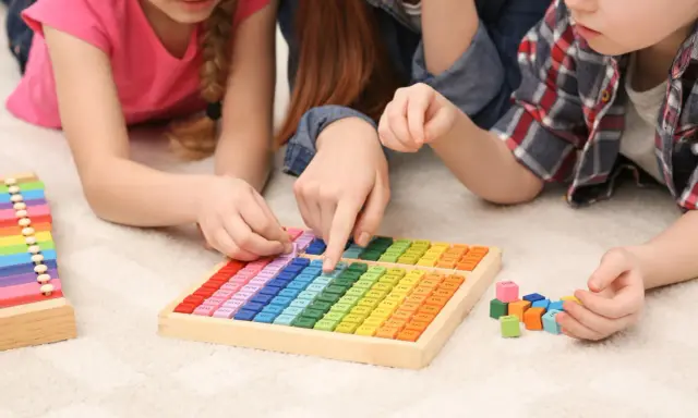 Kinder lernen spielerisch Mathe mit bunten Holzbausteinen und einem kleinen Abakus.