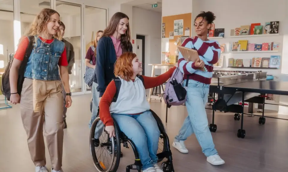 Schülerinnen gehen lachend durch den Flur. Eine im Rollstuhl, was **Inklusion an Schulen** zeigt.