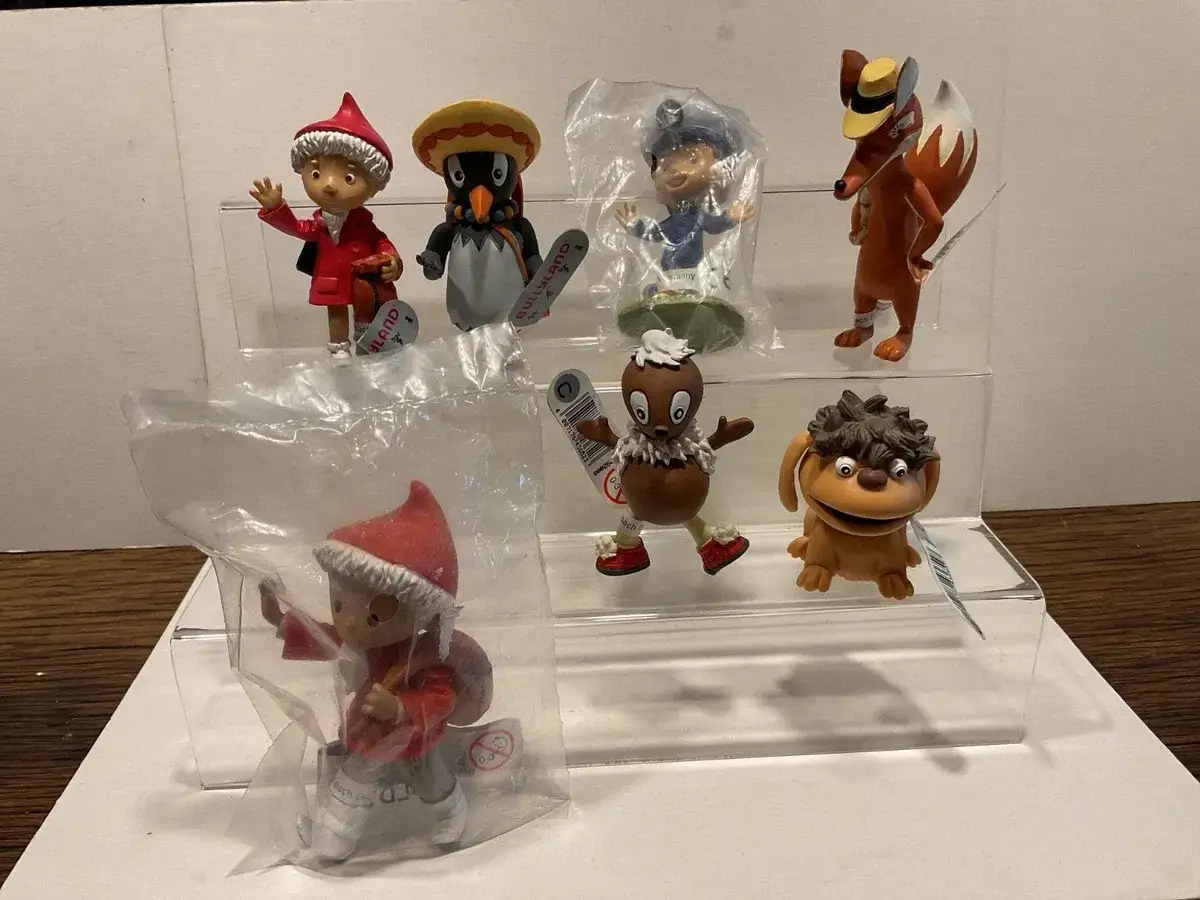Sammlung von Sandmann-Charakteren: Ein Junge mit rotem Mantel, ein Pinguin mit Sombrero, ein Polizist, ein Fuchs, ein Schokoladenmann und ein braunes Wesen.