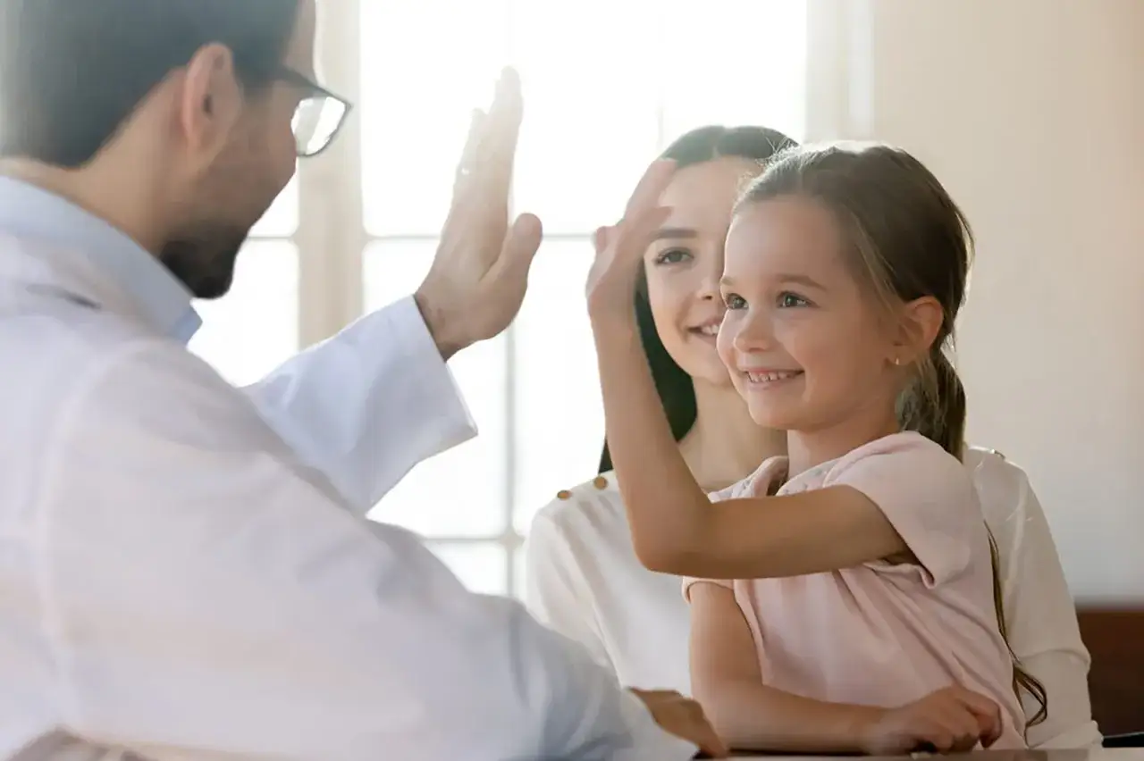 Arzt gibt Kind und Mutter High-Five. Ein Arzt kann Autismus feststellen, hier ein positives Beispiel.