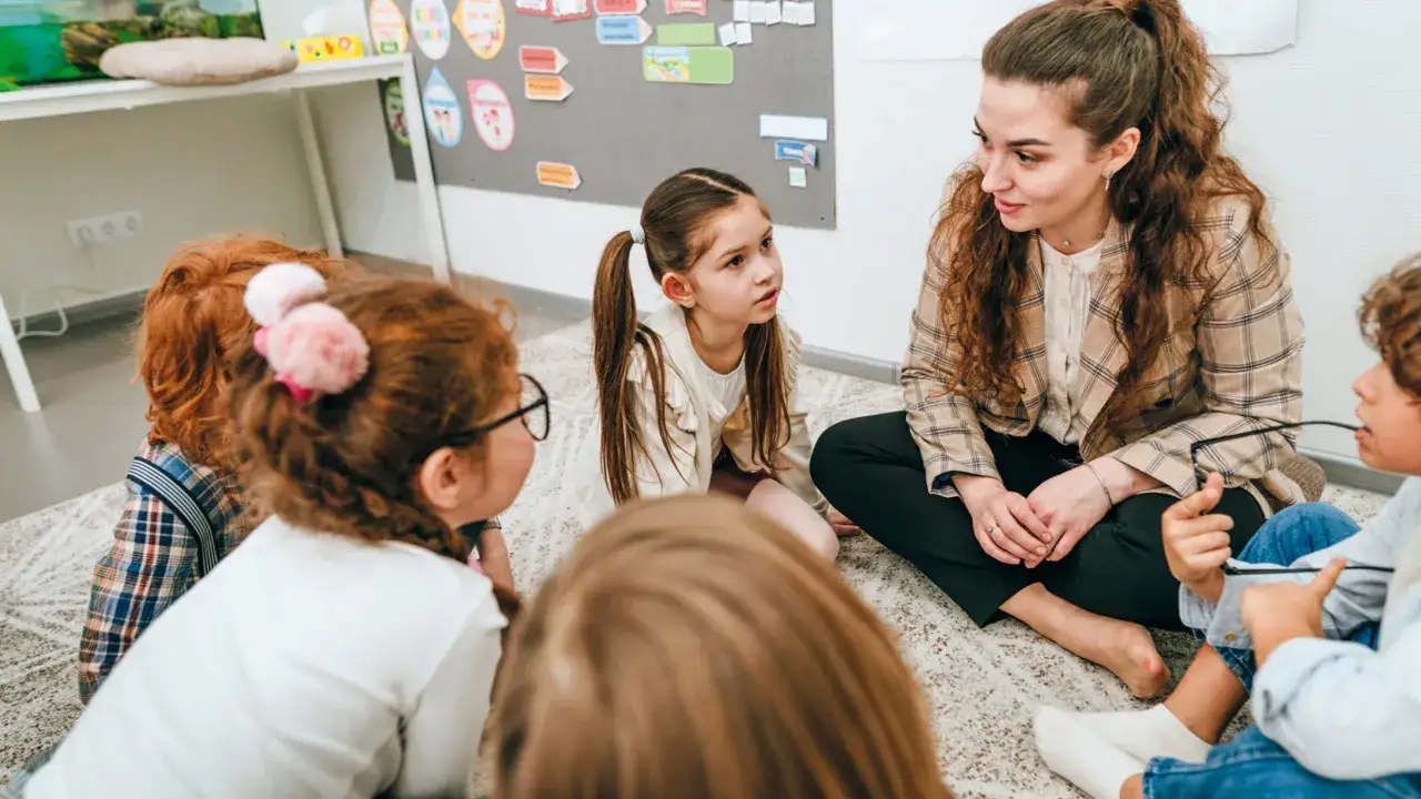 Lehrerin und Kinder philosophieren in der Grundschule. Sie sitzen im Kreis auf dem Teppich und diskutieren angeregt.