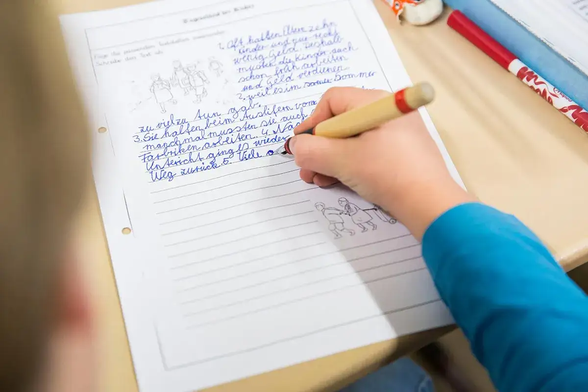 Kind schreibt mit schlechter Rechtschreibung und kleinen Bildern auf ein Blatt Papier.