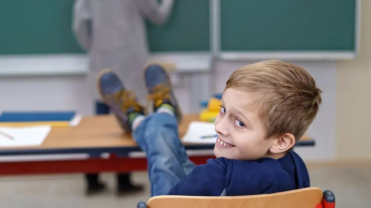Ein Junge mit frechem Grinsen im Unterricht. Der Umgang mit schwierigen Kindern in der Grundschule kann herausfordernd sein, aber auch lustig.