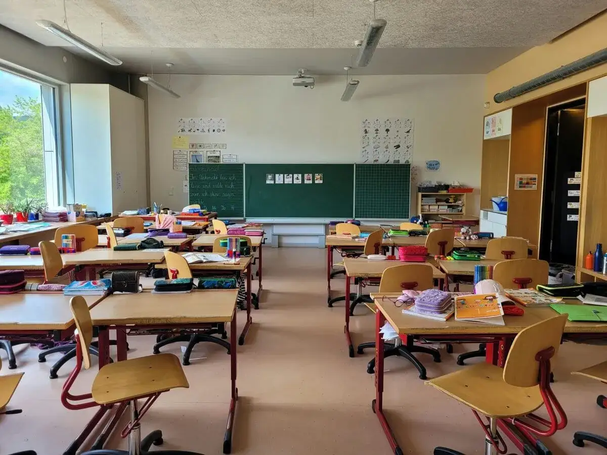 Leeres Klassenzimmer mit vielen Schultischen und Stühlen. Die Tafel ist beschriftet. Es herrscht eine friedliche Ruhe im Klassenzimmer.