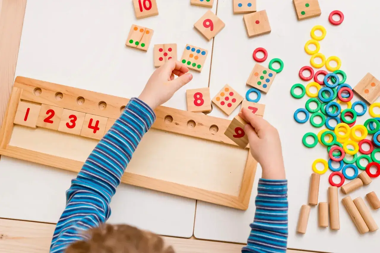 Kind spielt mit Holzbausteinen und Ringen, um das Rechnen zu lernen. Zahlen 1-9 sind sichtbar.