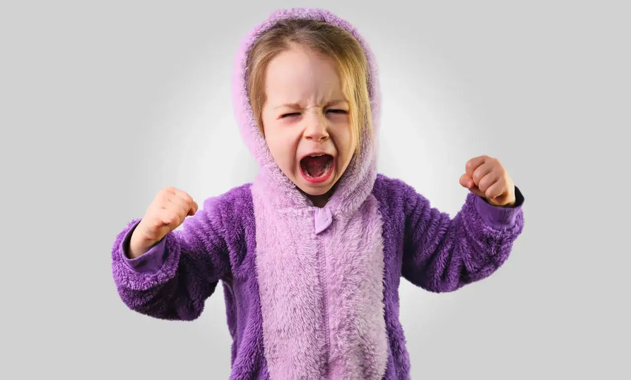 Kleines Kind im lila Pyjama schreit w&uuml;tend, F&auml;uste geballt. Ein Ausdruck starker Emotionen bei Kindern.