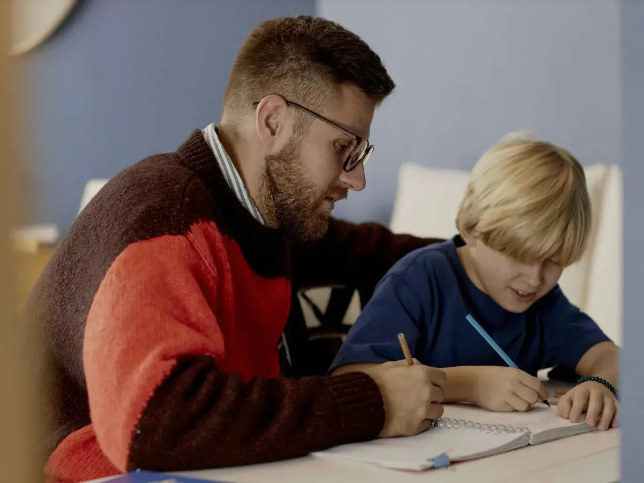 Ein Mann mit Brille hilft einem Jungen beim Lernen. Gemeinsam meistern sie Herausforderungen und lernen den Umgang mit Misserfolg.