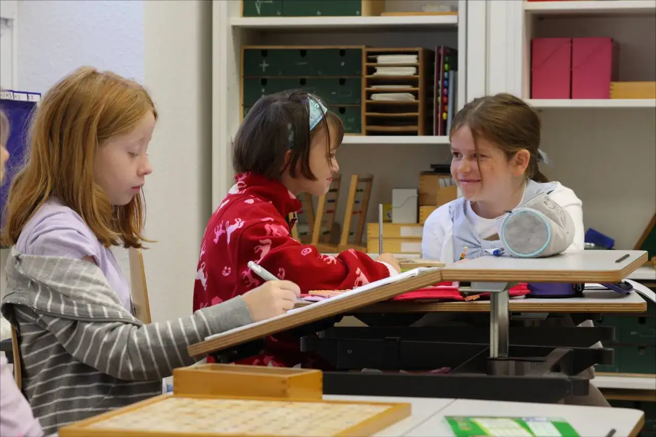 Drei M&auml;dchen in der Grundschule lernen und arbeiten konzentriert. Ein M&auml;dchen schreibt, die anderen unterhalten sich.